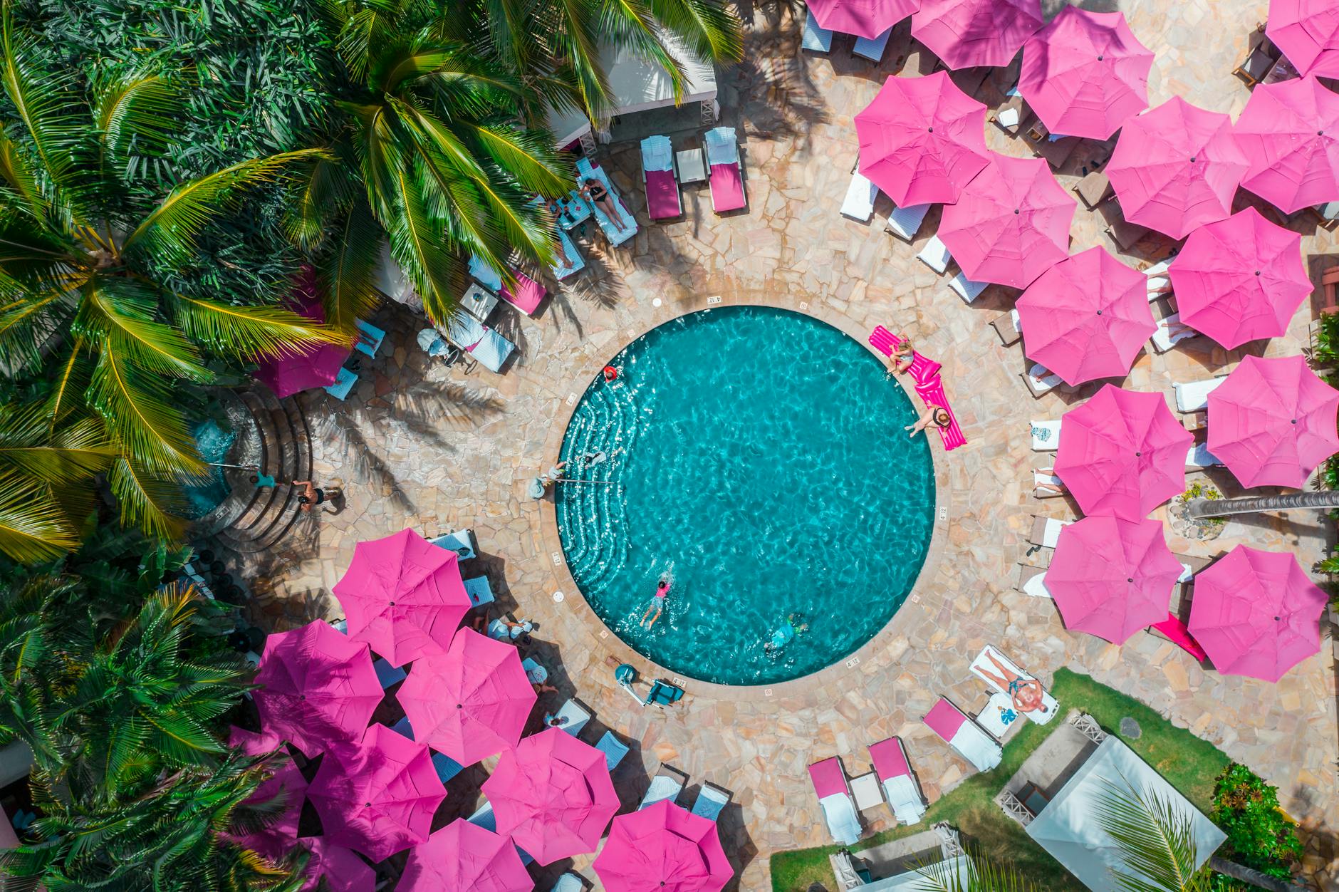 Aerial view of colorful Waikiki resort pool surrounded by pink umbrellas and lush palm trees